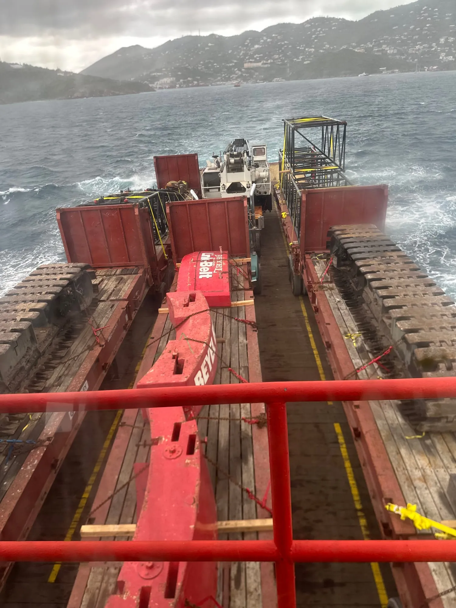 A crane boom strapped to the deck of a barge crossing open water to St. John