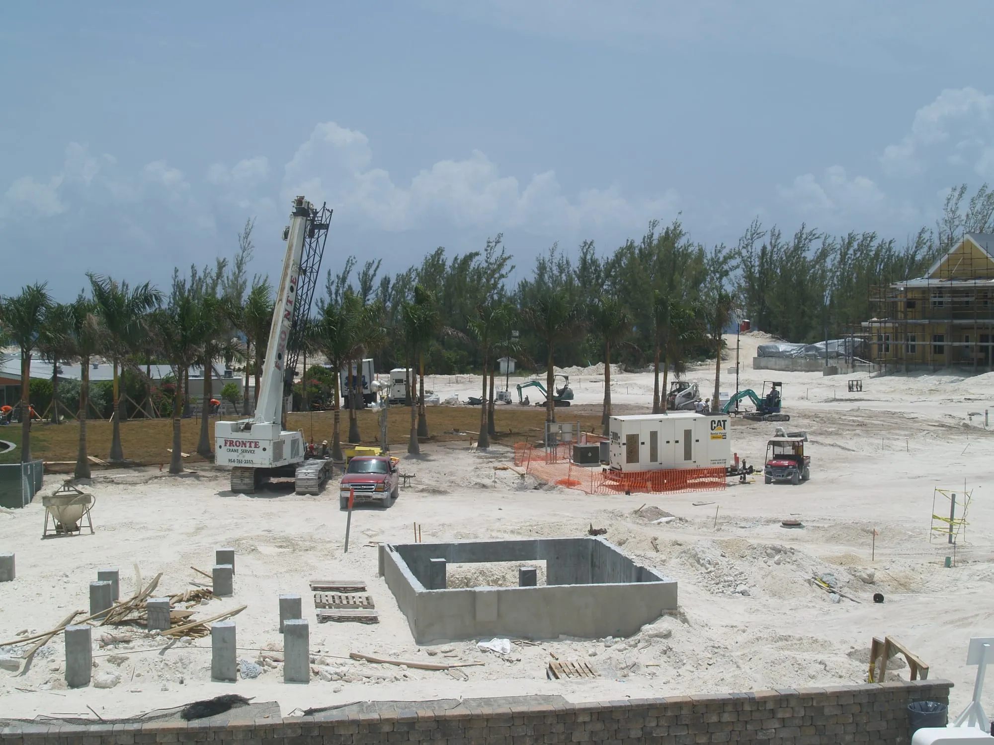 A crawler crane working over fresh foundations, with the frame of a further house behind