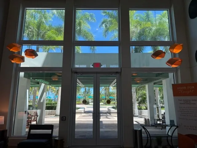 The lobby's full-height glazed wall looking out to the pool deck and the palms beyond